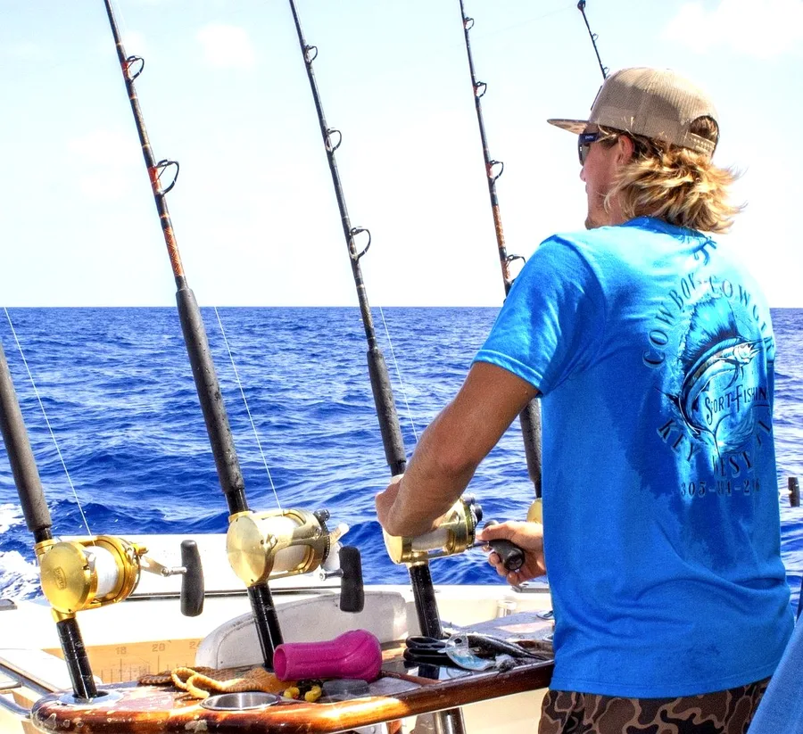 Cowboy Cowgirl crew member running trolling rods in deep blue offshore water near Key West