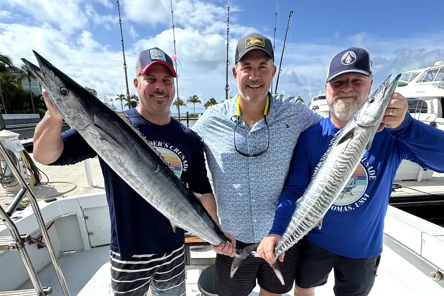 Three anglers holding kingfish on the deck at the marina