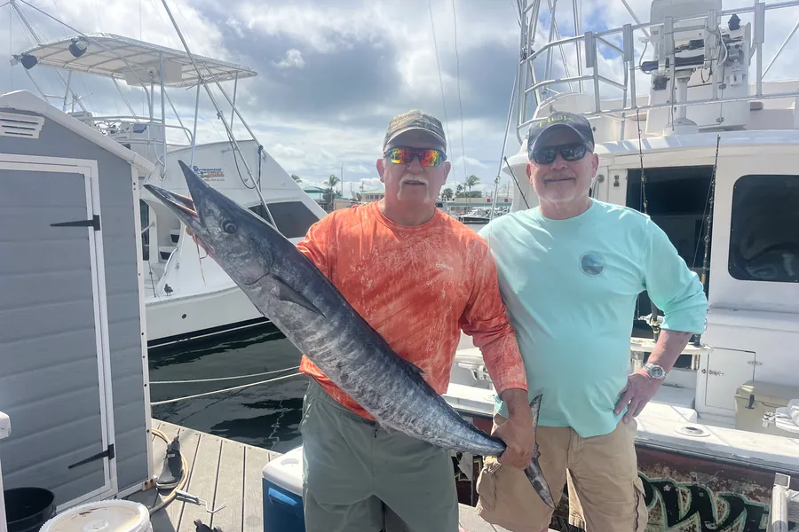 Two anglers holding a wahoo on the dock