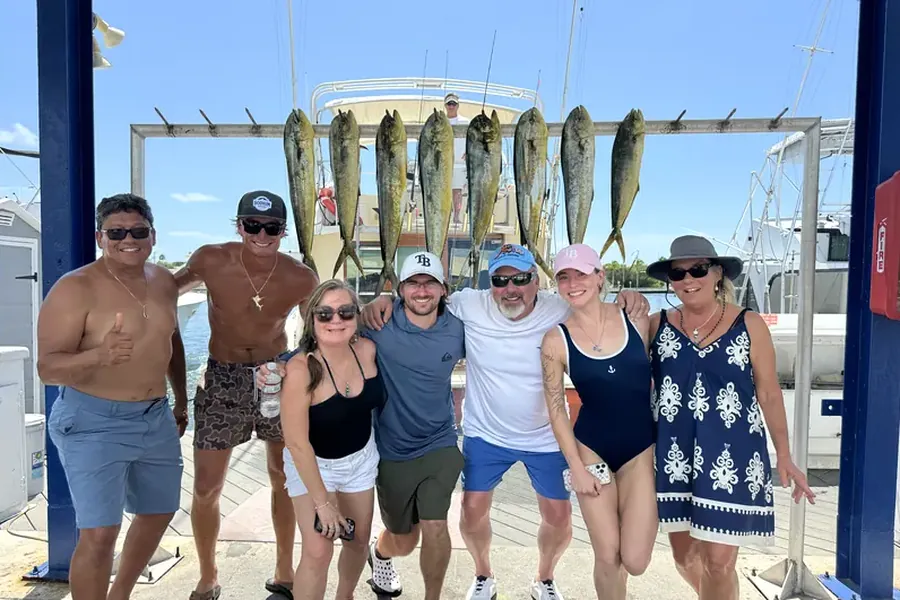 Group of happy anglers at the dock with their mahi-mahi catch on the rack behind them