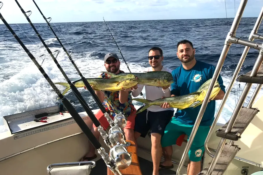 Three anglers holding mahi-mahi in the cockpit offshore of Key West