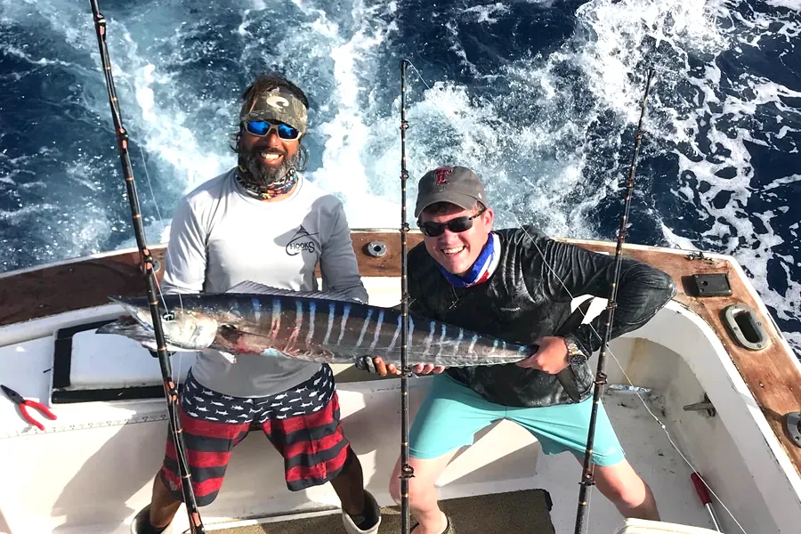 Mate and angler holding a striped wahoo in the cockpit